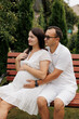 © Anhelina  - Expecting couple sitting on a bench in the garden. Pregnant woman in white dress with her partner embracing gently. Cozy family photo shoot full of love, tenderness, and harmony.