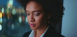 © Videophilia - Thoughtful woman looking down, standing by a window with glowing bokeh city lights, contemplating future business strategies in an urban office setting at night
