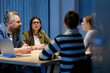 © .shock - Group of diverse coworkers having a serious discussion around a conference table, led by a bearded male manager, representing teamwork, leadership, and strategy development in a modern business