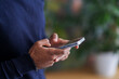 © Studio Marmellata - Crop anonymous Arab male in warm sweater messaging on cellphone while standing against blurred houseplants at soft daylight