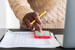 © Studio Marmellata - Crop anonymous black male in casual sweater with documents and pencil using smartphone counting bills on calculator