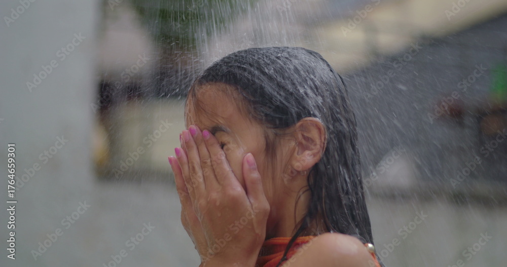 Young girl splashing water on her face under an outdoor shower on a ...