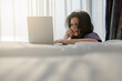 © shine - Good morning, Happy smillingasian middle aged woman sitting bedside in air conditioner room enjoying fresh air, working on laptop by window with natural light. Exuding confidence and style. Copy space