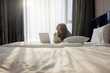 © shine - Middle-aged woman eating popcorn and watching movie on laptop. Warm sunlight is streaming through sheer curtains into a cozy bedroom, creating a peaceful and inviting atmosphere in the early morning.