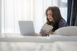© shine - Happy satisfied mature woman eat popcorn watch movie film on laptop at home or hotel, relax spend free spare time in bedroom. Natural sunlight streaming through the window, refreshing atmosphere.