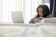 © shine - Positive asian middle aged woman with long hair, holding a coffee cup while using a laptop at home for online shopping or freelance work as sunlight fills the cozy bedroom.