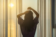© shine - Young woman styling hair with a claw clip ,easy daily hairstyling. Woman standing at window in bedroom and fresh wake up with sunrise in hotel or home ready for day. View and nature on holiday.