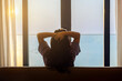 © shine - Weekend at home. Relaxed middle aged woman sitting on comfortable couch in cozy living room holding hands behind head, Enjoying nature, Sunlight through the window in room. Beautiful sky background.