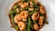 ©  AugmentArt - Garlic shrimp and asparagus stir fry served on a white dish with oyster sauce, overhead shot.