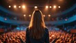 © miss irine - Female speaker addresses large audience in modern auditorium. Woman stands on stage with hands open, presenting to many people. Public speaking event delivers motivational talk business seminar.