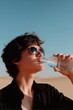 © Konstiantyn Zapylaie - Young caucasian female drinking water in desert sun wearing sunglasses