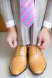 © Konstiantyn Zapylaie - Caucasian male adult tying brown leather shoes with striped suit and pink striped tie