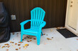 © scandamerican - A single blue plastic Adirondack style chair, along with a few autumn leaves and a mat on the cement patio.