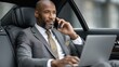 © scaliger - Smiling black man in formal suit sitting in car, african american businessman talking on phone using laptop