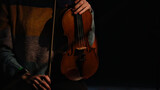Close up of violinist hands with wooden string instrument illuminated by stage lights creating intimate concert atmosphere with copyspace