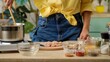© kinomaster - A woman in a yellow shirt and jeans is cooking in a kitchen with various ingredients and spices on the counter. Preparing lunch or dinner in a home kitchen.