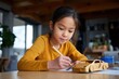 © Iryna - Asian young girl drawing near wooden car in sunlit room