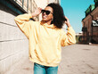 © halayalex - Beautiful woman with afro curls hairstyle.Smiling hipster model in yellow hoodie. Sexy carefree female posing on the street background in sunglasses. Cheerful and happy