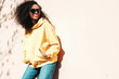 © halayalex - Beautiful woman with afro curls hairstyle.Smiling hipster model in yellow hoodie. Sexy carefree female posing on the street background in sunglasses. Cheerful and happy