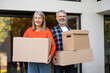 © zinkevych - Smiling senior couple carrying cardboard boxes at home entrance