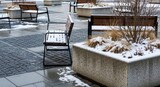 Winter urban scene with snow-covered benches and planters in a concrete plaza