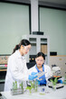 © laddawan - Asian food scientists in lab coats analyze vegetables with microscope for biotech, nutrition, and safety testing. Lab tubes, gloves