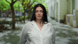 © Krakenimages.com - Woman in white shirt standing outdoors on a city street, surrounded by trees, showcasing urban fashion and confident expression with greenery background.