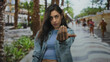 © Krakenimages.com - Young woman beckons with outstretched hand toward camera on street promenade lined with palm trees and buildings; assertive invitation.