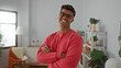 © Krakenimages.com - Young man in a red sweater and glasses smiling confidently with crossed arms in a bright indoor room featuring cozy decor and plants.