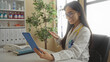 © Krakenimages.com - Doctor holding tablet during video call in hospital room, smiling warmly, surrounded by medical equipment and office furnishings, reflecting a professional healthcare environment.