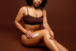 © deagreez - Tender black woman with natural hair applying skincare cream while posing on a brown background