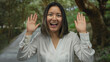 © Krakenimages.com - Woman smiling joyfully with hands raised in a serene park, showcasing youthful energy and happiness in a lush outdoor setting.