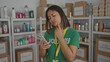 © Krakenimages.com - Woman in green volunteer shirt uses smartphone in donation center surrounded by organized supplies on shelves suggesting volunteer work and community service.