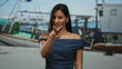 © Krakenimages.com - Woman gesturing with fingers at seaside port, wearing navy dress, with boats in the background, capturing a casual outdoor setting along the coastline.