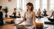 © Katlin - Young serene woman in lotus pose meditating during a group yoga class in a bright fitness studio. Concept of mindfulness, wellness, relaxation, mental health, balance, and harmony.
