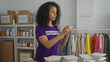 © Krakenimages.com - Woman volunteering indoors takes photo in charity center with donation boxes and clothes rack.