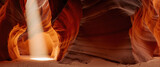 Red sandstone slot canyon glows in deep orange hues. A magical beam of sunlight illuminates the path through the narrow passage.