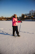 © StockMediaSeller - Elderly woman in a pink jacket walking with trekking poles across a snowy field on a sunny winter morning. She enjoys outdoor exercise and fresh air in a calm rural landscape.