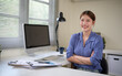 © matinee - Smiling young woman standing with folded arms at her desk, feeling positive and professional.