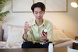 © matinee - Man sitting on sofa reading pill bottle label before taking medicine. Concept of health care, treatment, and daily medication.
