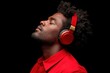 © Valentyna - A young Black man with curly hair listens to music with red headphones, eyes closed, enjoying a peaceful moment
