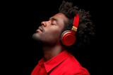 A young Black man with curly hair listens to music with red headphones, eyes closed, enjoying a peaceful moment