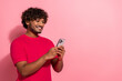 © deagreez - Young man in red t-shirt holding smartphone while smiling, standing against pink background exhibiting casual style fashion