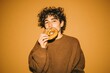 © olegganko - Young Person Enjoys a Large Pretzel Against a Warm Orange Background While Smiling Happily