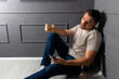 © Marko - Man sitting against wall holding drink while looking at phone in dimly lit room