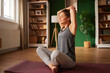 © Stockphotodirectors - A woman sits on a yoga mat in a bright living room, performing a stretching exercise. Sunlight filters through the window, creating a calm and peaceful atmosphere.