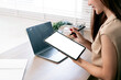 © NAMPIX - Close-up of an Asian woman using a stylus pen on a blank screen digital tablet mockup with a laptop on the desk.