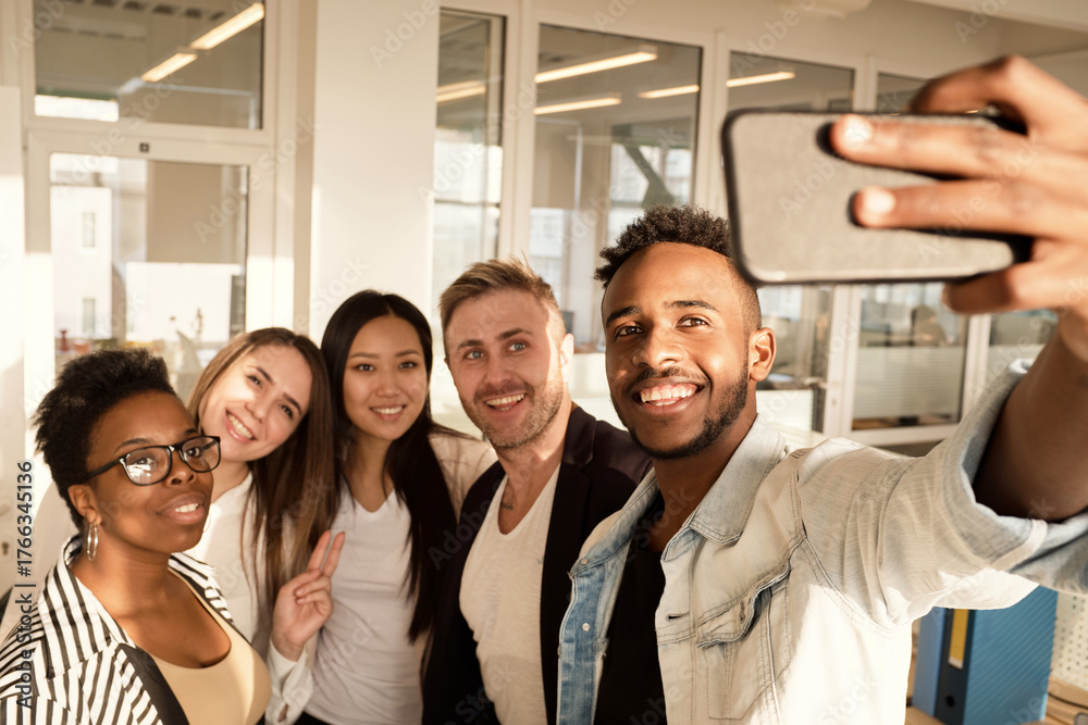 Multiethnic group of young colleagues smiling happily at smartphone ...
