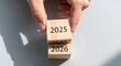 © Design - Hand flipping wooden blocks from 2025 to 2026, representing the passage of time, new year transitions, future planning, and setting strategic goals for the upcoming period