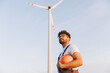 © anatoliycherkas - Technician holding helmet looking up at wind turbine in sustainable energy plant